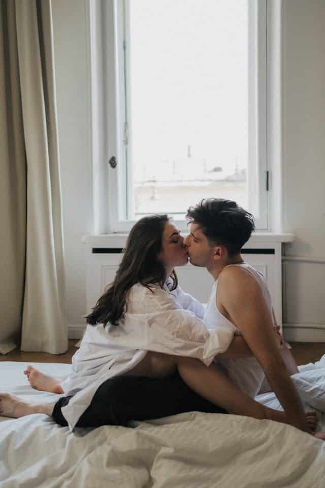 couple kissing in bed by the window
